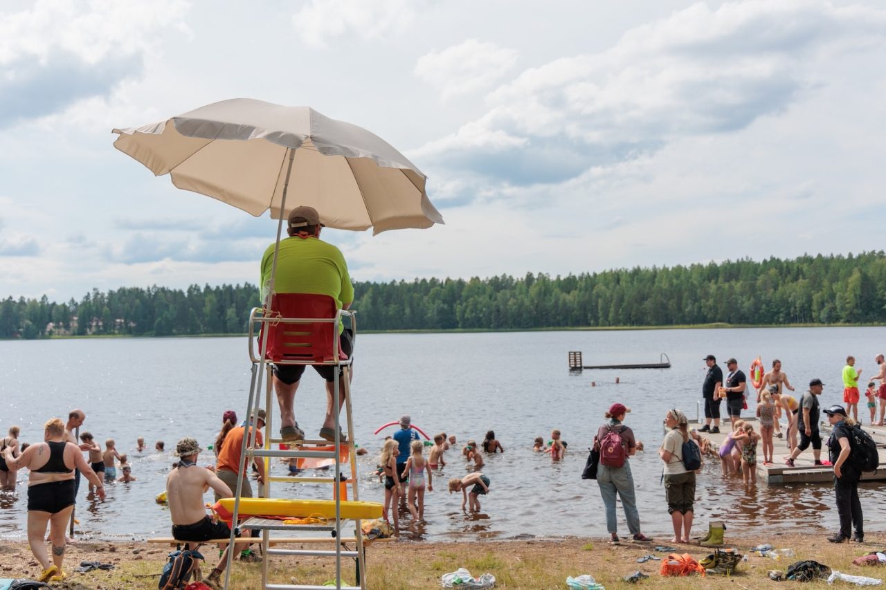 Uinninvalvoja istuu aurinkovarjon alla hiekkarannalla.