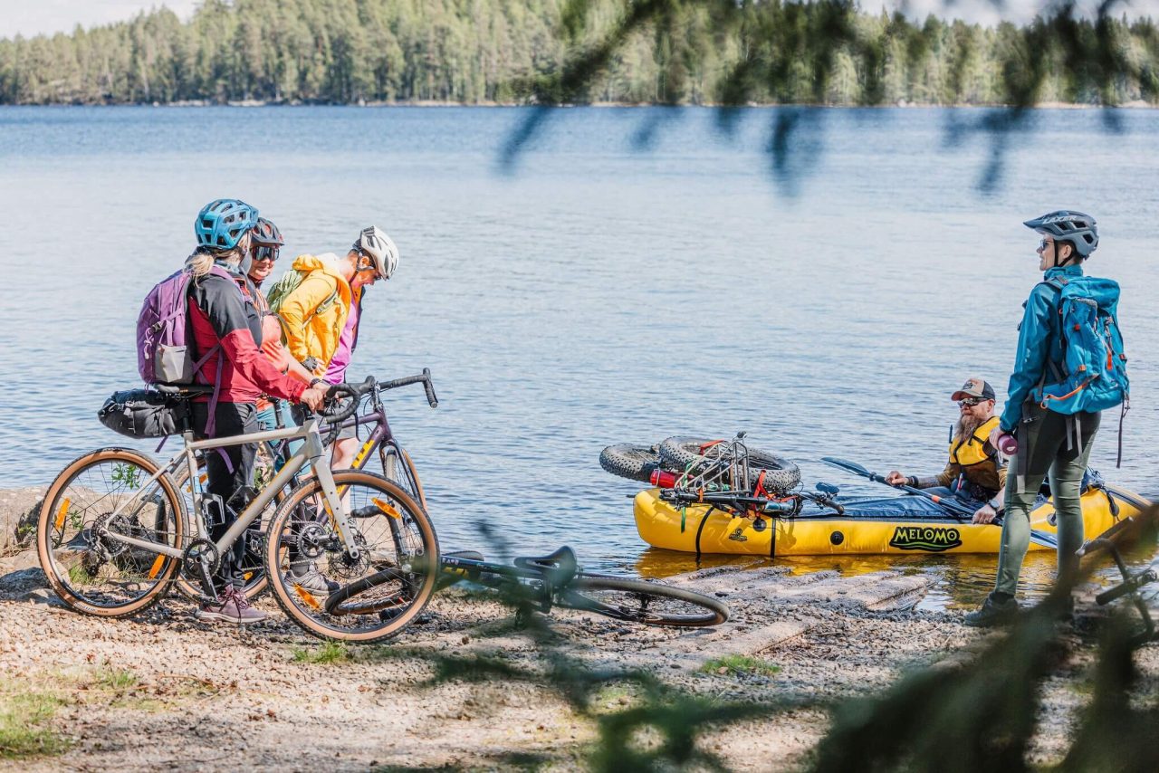 Kanootilla meloja on rantautunut järvellä paikkaan, jossa Häme by cycle gravel ja bikepacking pyöräilijät ovat.