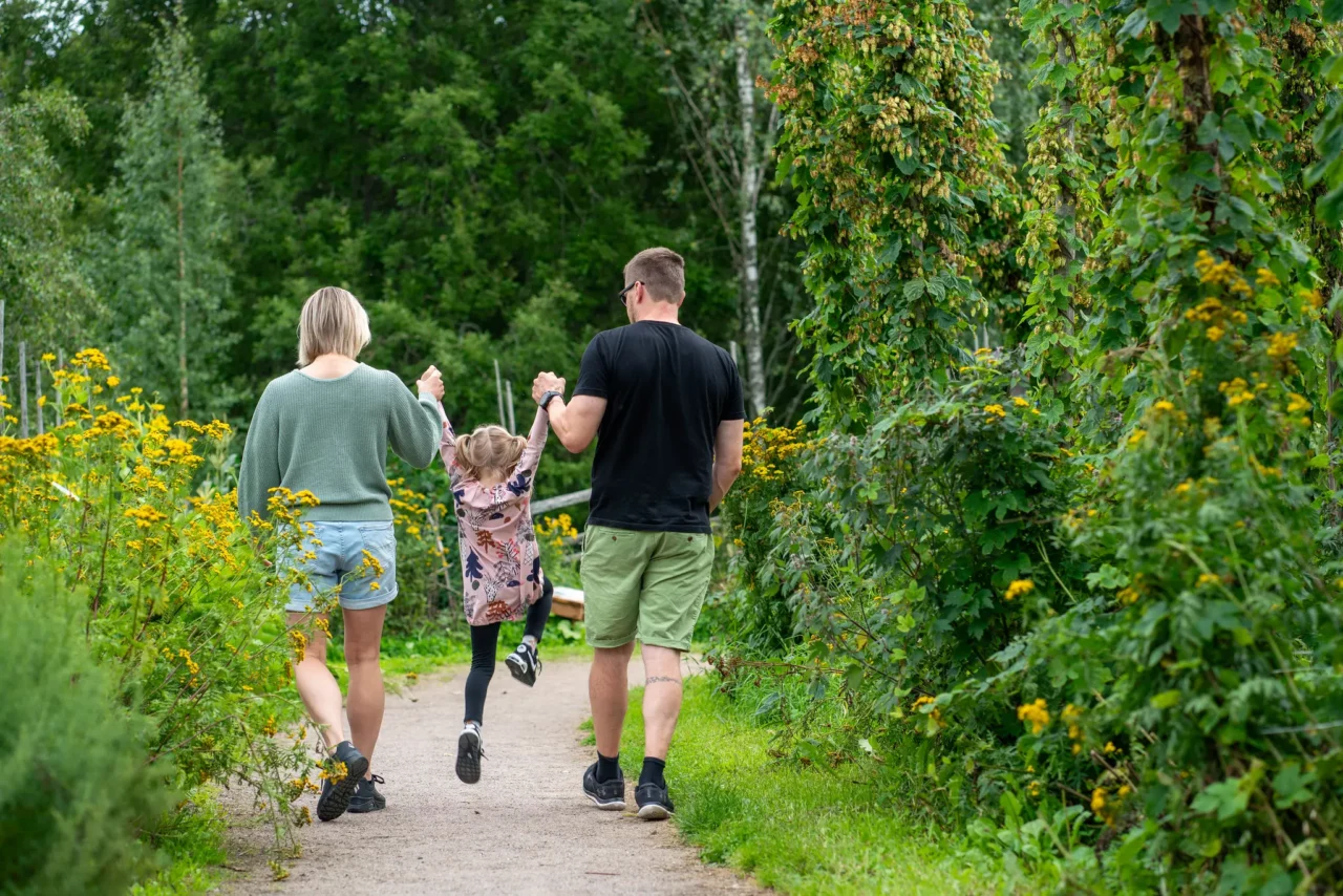 Vanhemmat ovat tyttären kanssa luonnossa. He pitävät tyttären kädestä kiinni ja nostavat tätä.