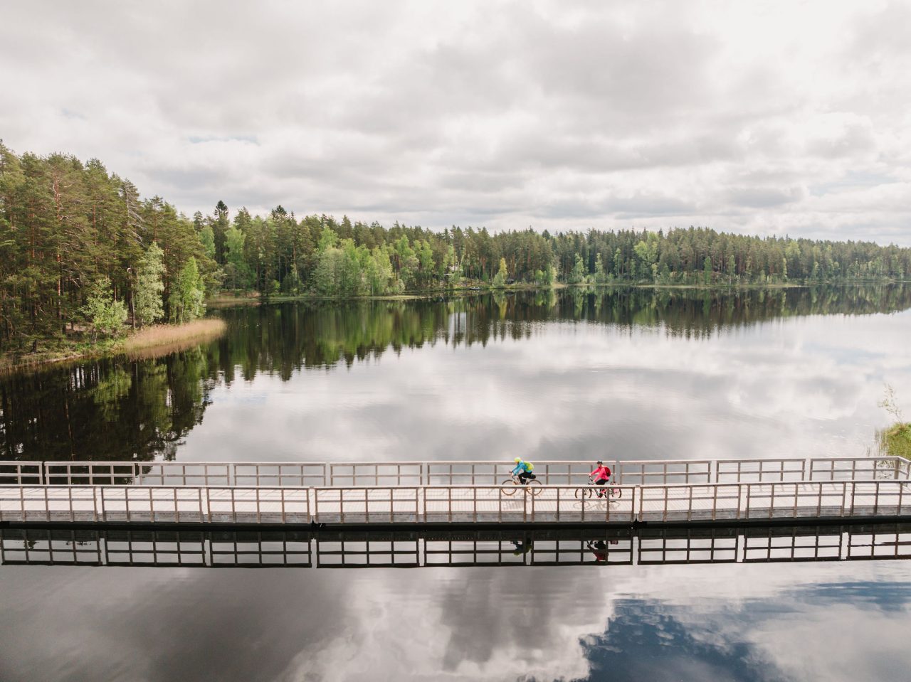 Kaksi pyöräilijää sillalla, joka kulkee järven päältä.