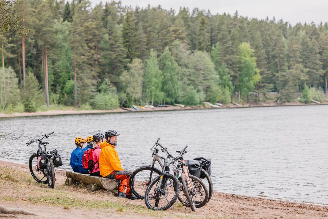 Perhe istuu penkillä ja katselee järvenrantamaisemaa.