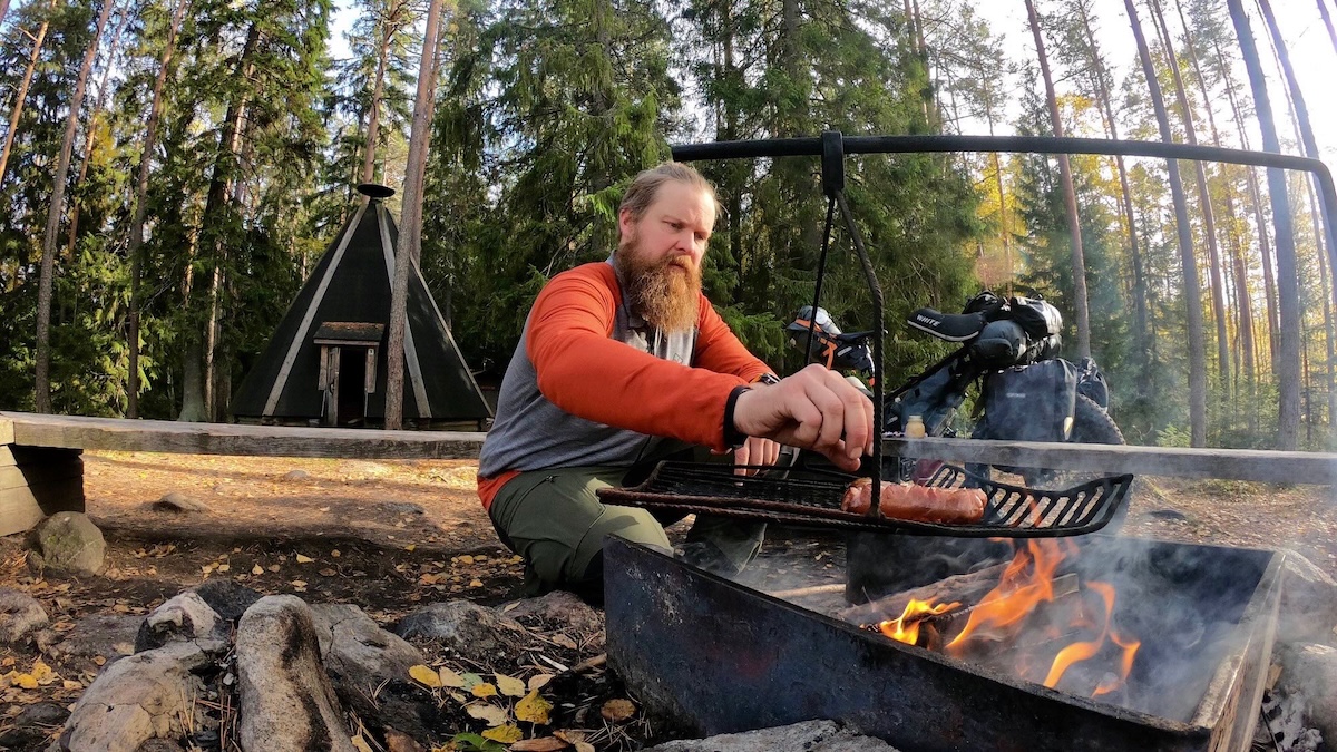 Mies paistamassa makkaraa kodalla. Hän on pyöräretkellä.