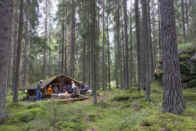 Ihmiset istuvat laavulla metsässä syömässä.