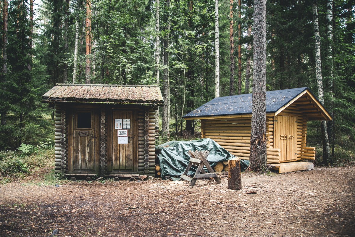 Puinen kuivakäymälä metsässä. Käymälän takana on puuvaja.