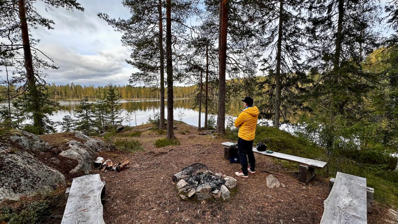 Mies seisoo nuotion vieressä ja katselee järvelle.