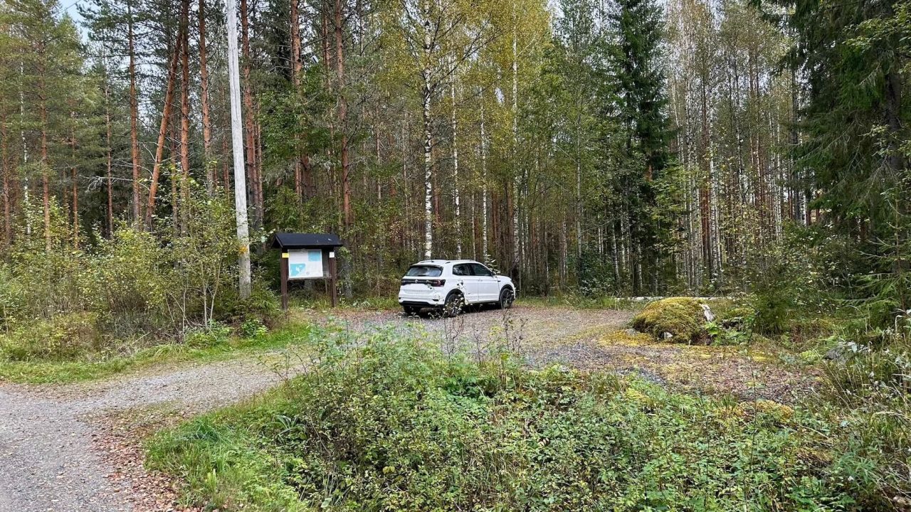 Pysäköintialueella on opastekyltti ja yksi auto.
