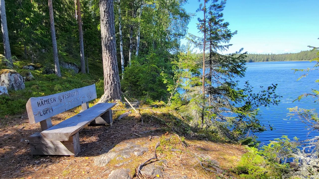 Hämeen Ilvesreitin maiseman katseluun ja taukoon tarkoitettu penkki Kivisammaljärven kierrolla Lopella. Järvinäköala, jossa taustalla metsä.