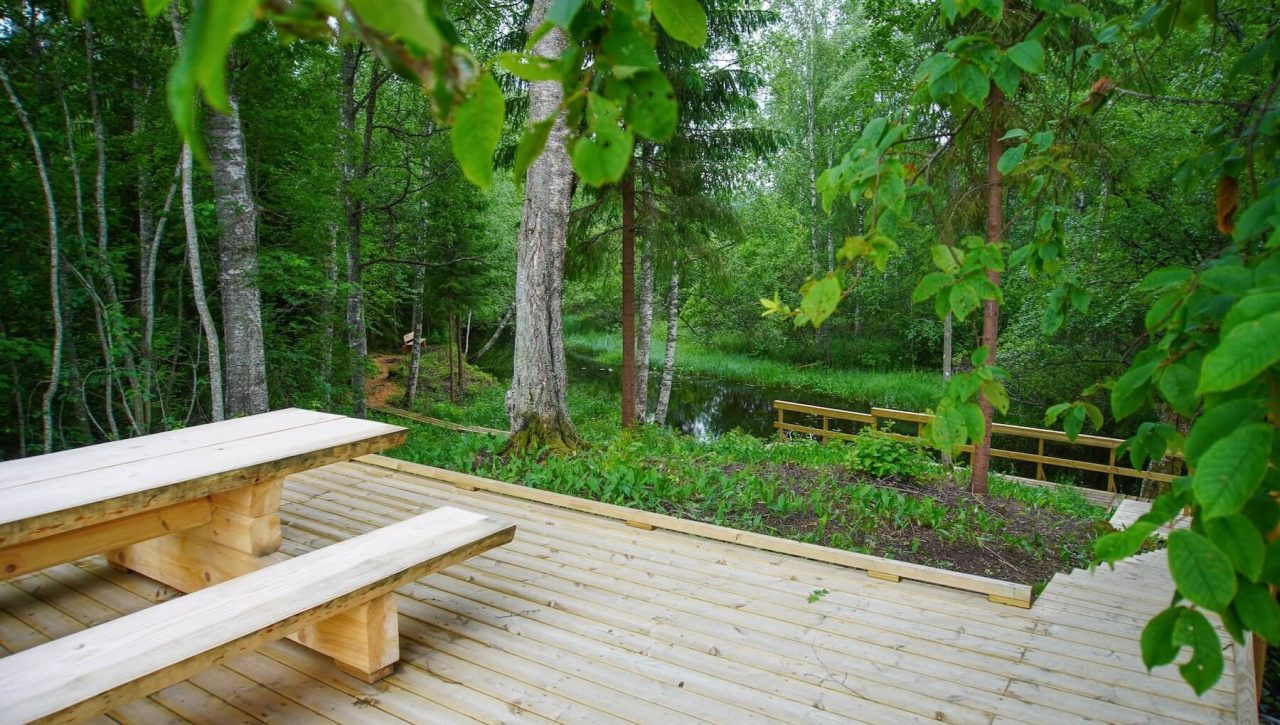Puisella terassilla on pöytäpenkkiyhdistelmä. Teraailta lähtee alas joen varteen portaat.