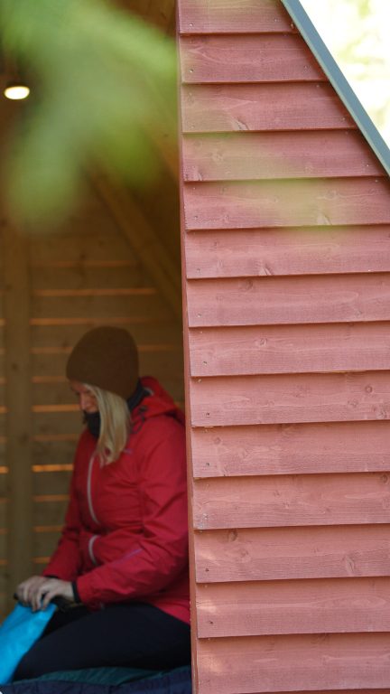 Nainen pakkaa rinkkaa punaisessa puusta rakennetussa teltassa.