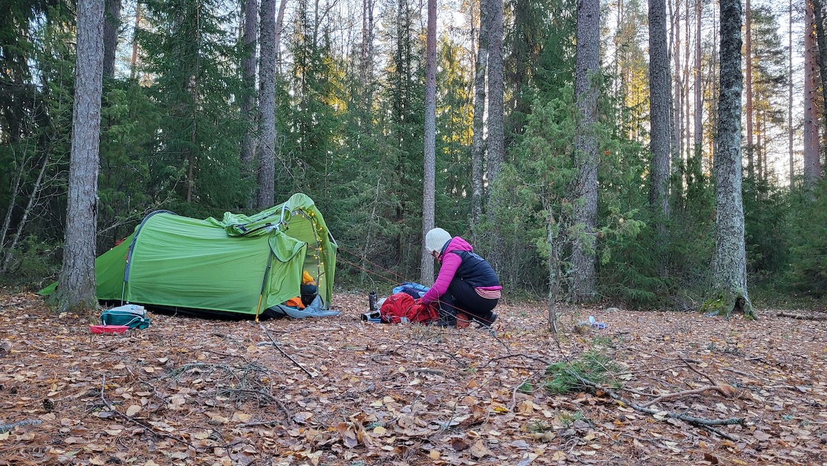 Nainen pakkaa telttaa metsässä.