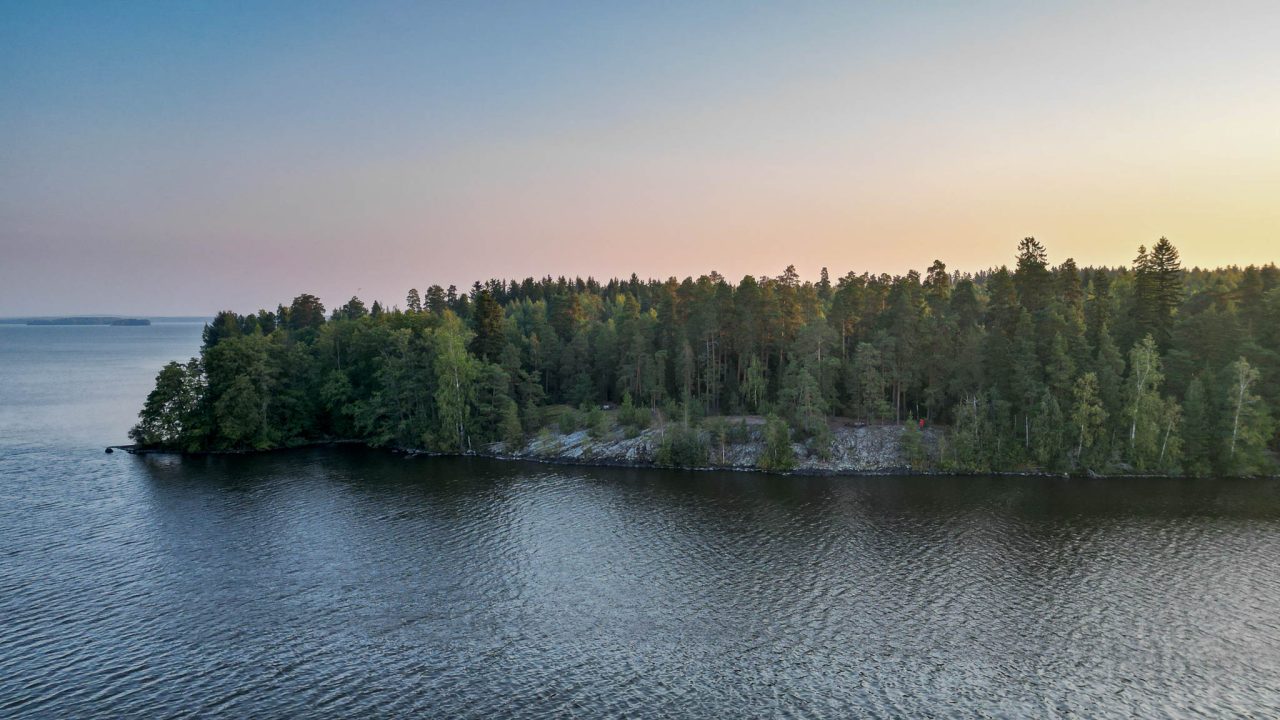 Auringonnousun värit taivaalla, edustalla järven ympäröimä niemi.