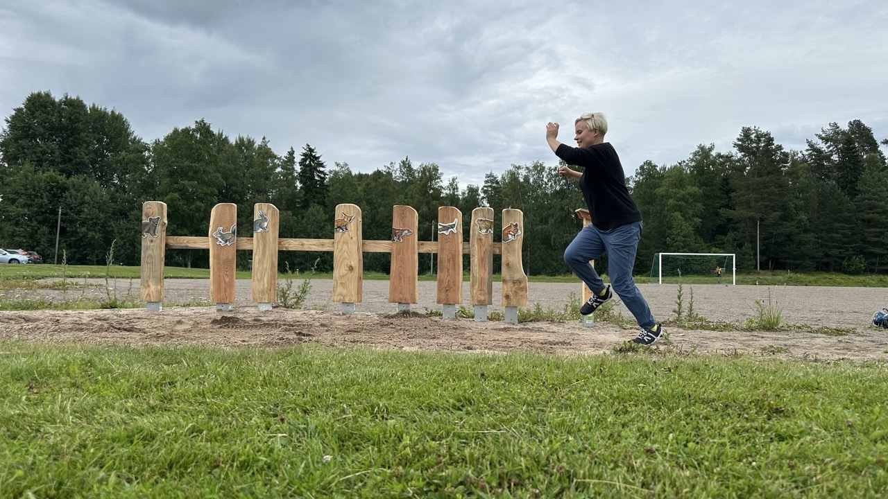 Ihminen hyppää pituutta ja kentän laidalla on eläinten kuvia eri kohdissa.